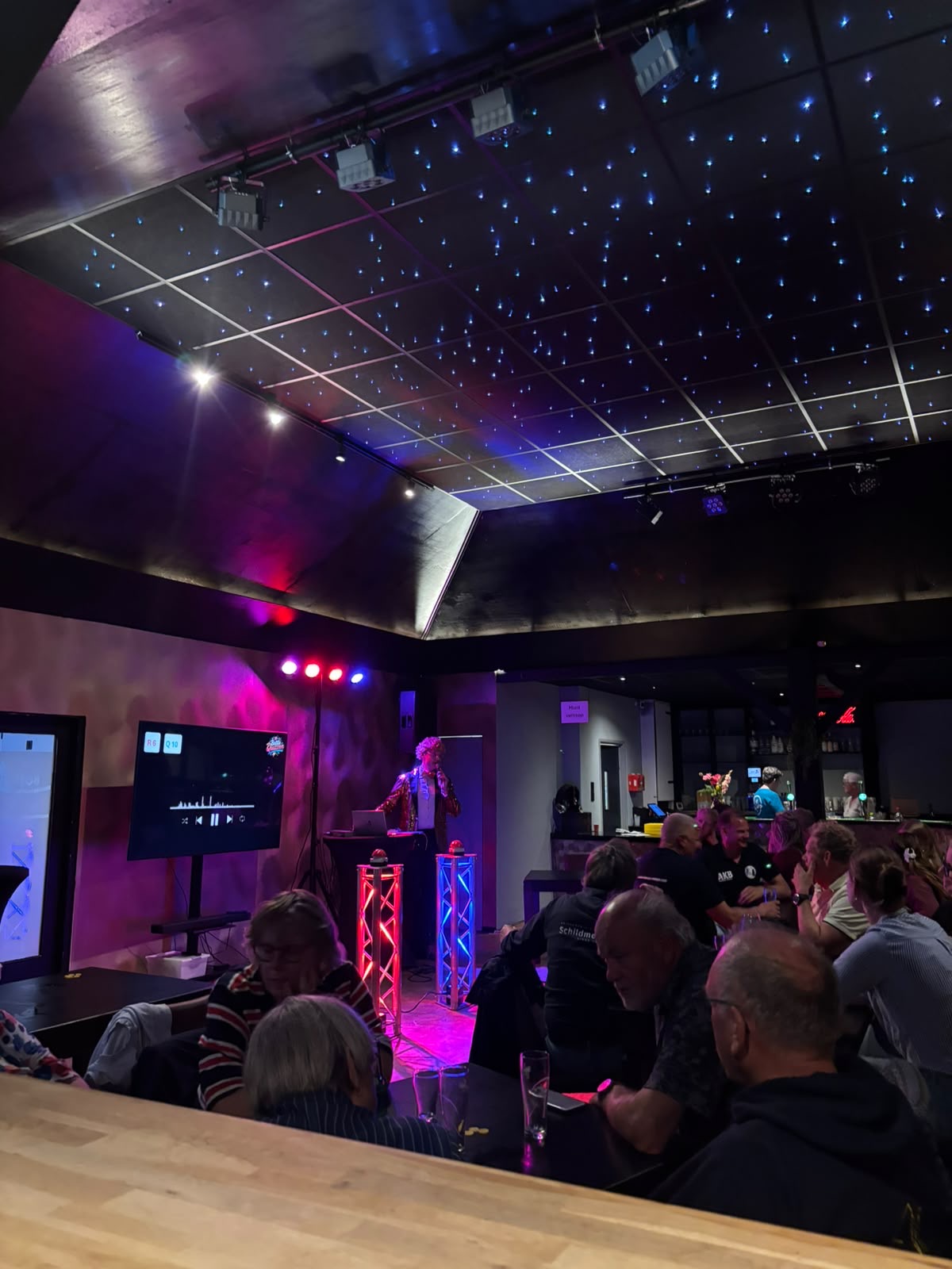 Publiek geniet van een Battle Quiz in een sfeervolle zaal met paarse belichting en sterrenhemel
